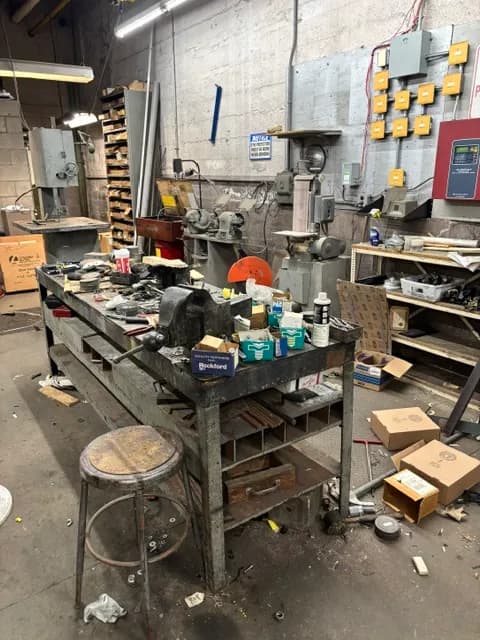 A machine-shop workbench with a bench vise, grinders, and hand tools.