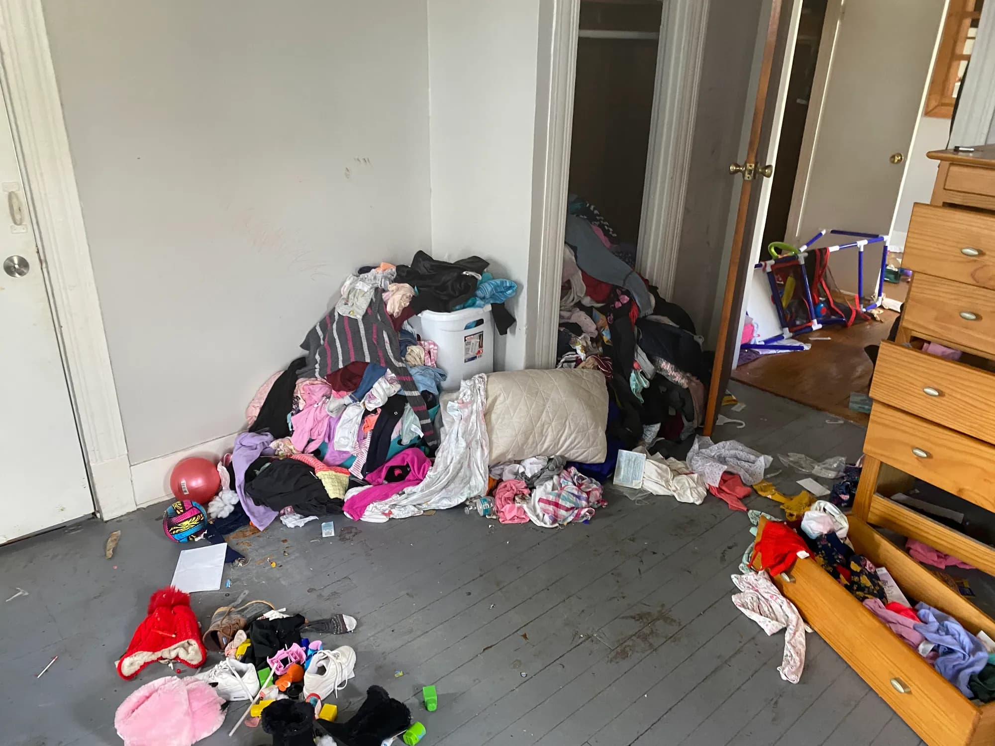 A bedroom with a pile of clothing in the corner and toys on the floor.